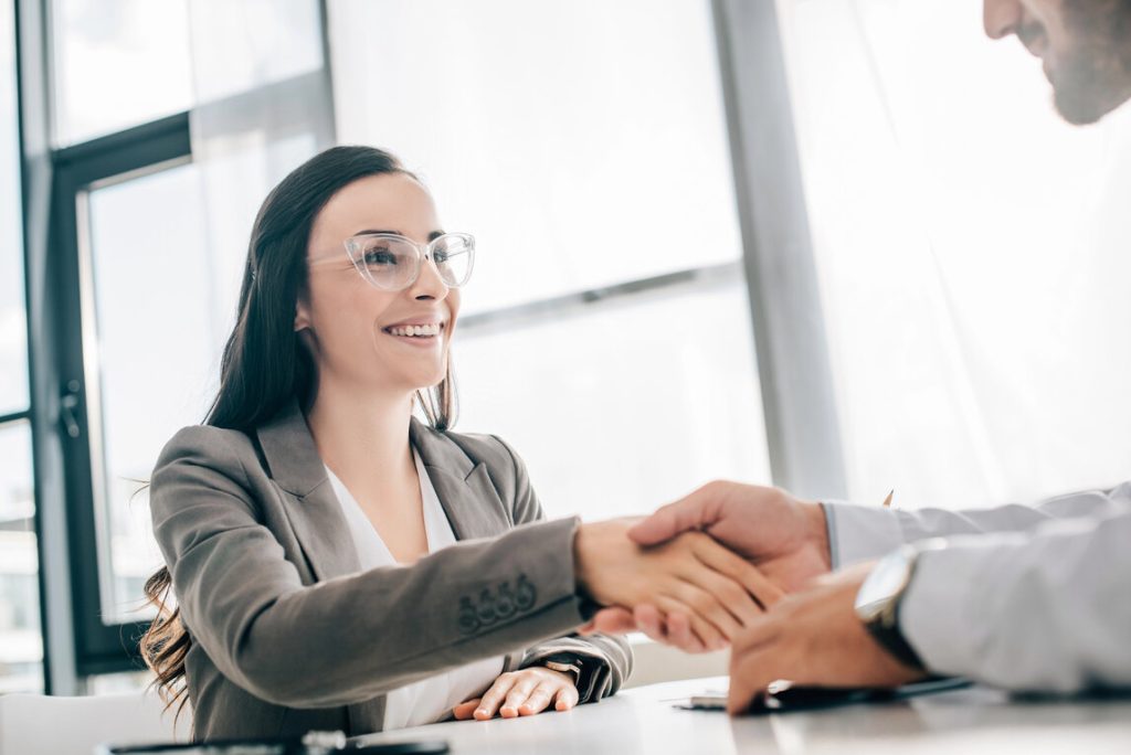 A woman in a business suit shakes hands with a man in a professional setting, symbolizing a business agreement