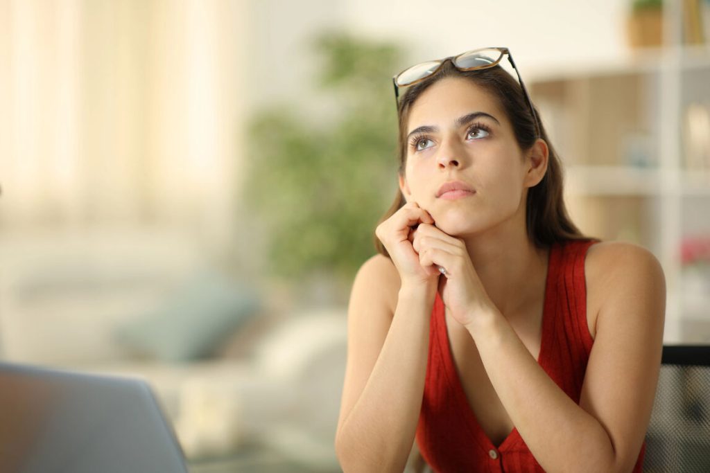 A woman with glasses intently looks at her laptop, possibly working or researching something online