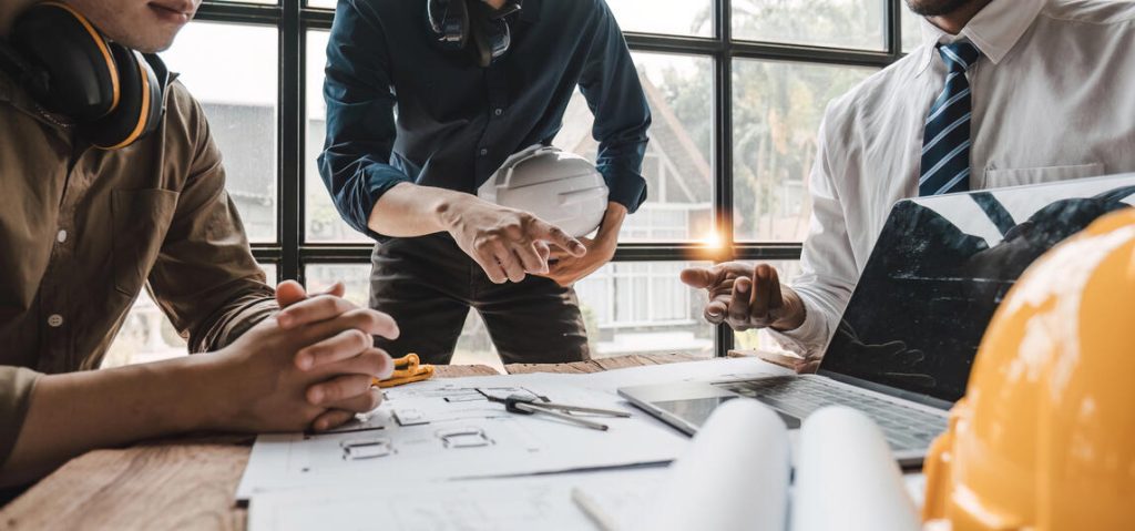 Three professionals in hard hats working together on a laptop, suggesting teamwork in a construction or engineering context