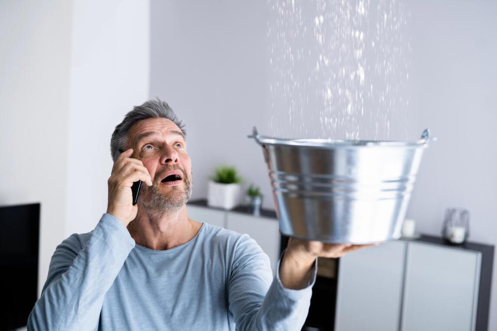 A man is talking on his cell phone, holding a bucket of water in his other hand, focused on his call