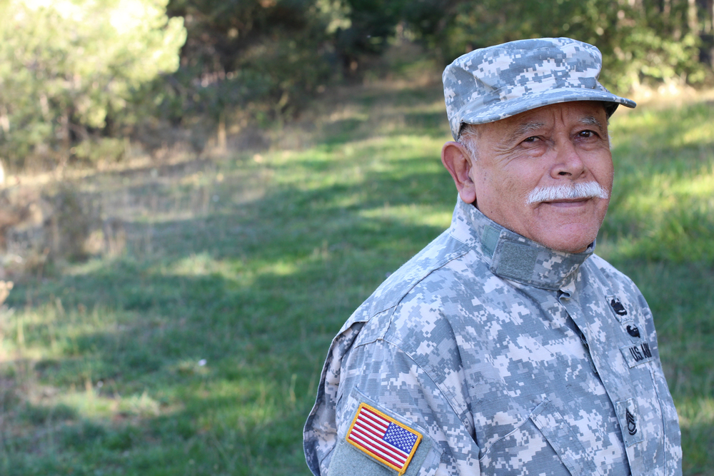 A 52-year-old veteran named Ahmed stands in a field, wearing a military uniform.