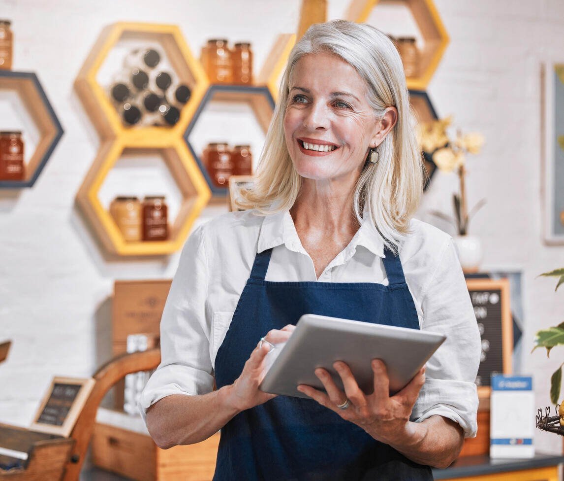 An entrepreneur in an apron is holding a tablet, symbolizing her engagement in business and technology. 