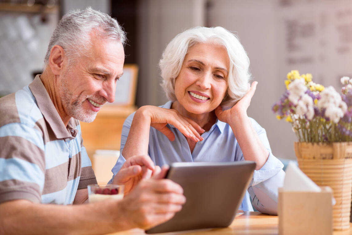 An elderly couple, both retirees, focused on a tablet computer in a cozy setting.