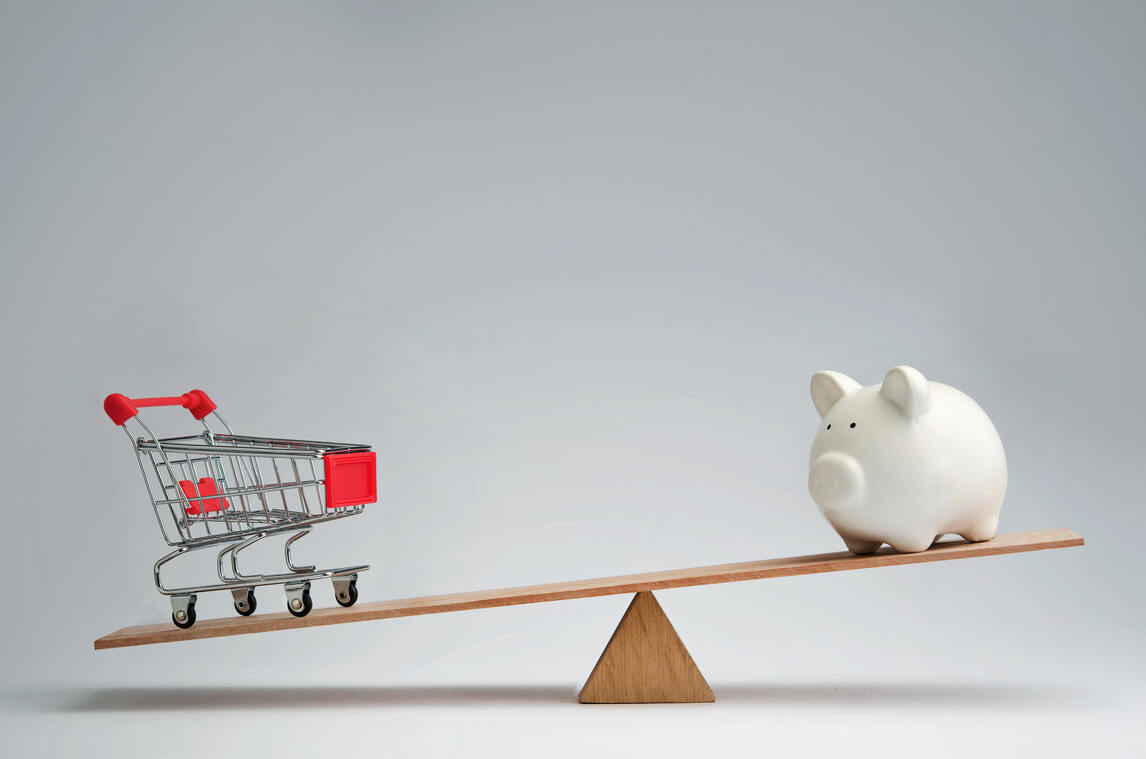 A piggy bank and shopping cart on a seesaw, illustrating the balance between savings and spending amid rising inflation.